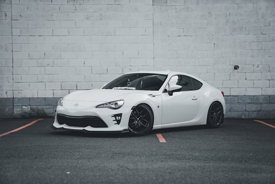 A stylish white sports car parked against a gray brick wall in a parking lot.