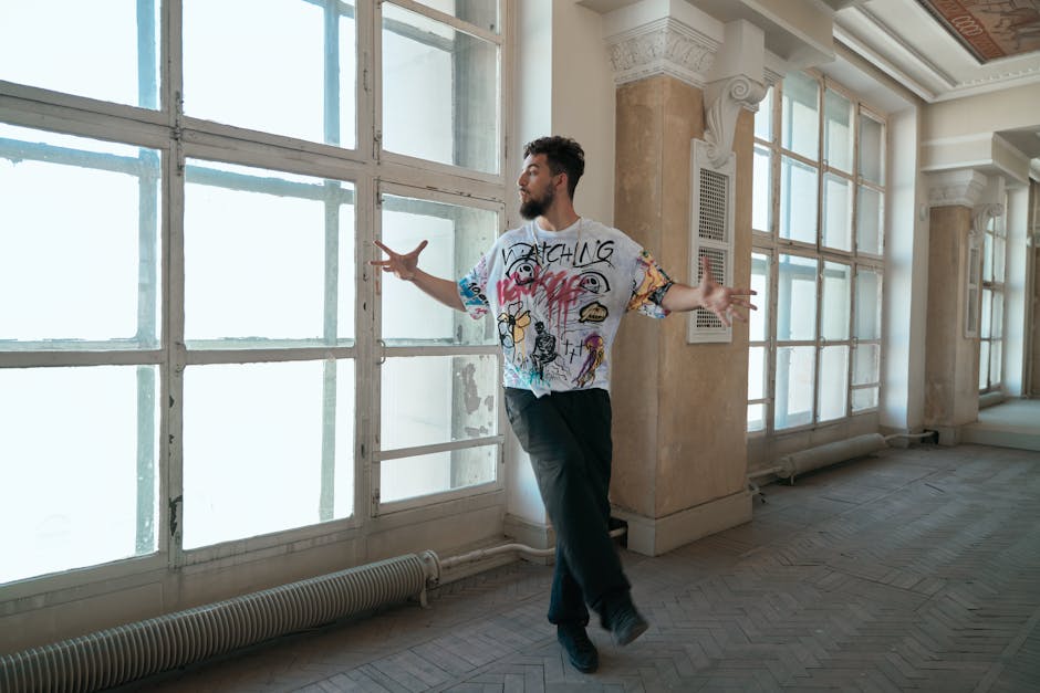 Male dancer performs a modern dance move in a sunlit room with large windows.