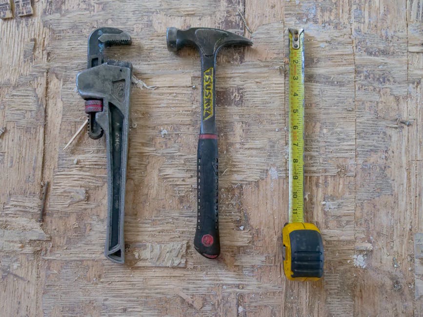 Close-up of hammer, wrench, and measuring tape on wooden surface for construction use.