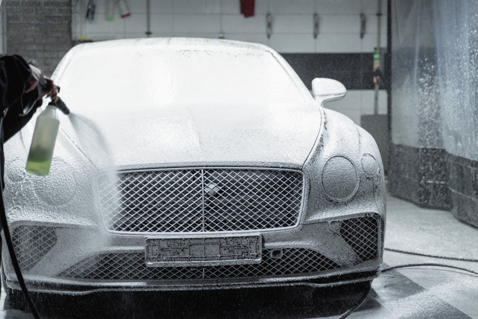 A luxury car is covered in foam during a detailed wash inside a garage.
